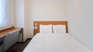 Quarto de hotel com cama, escrivaninha e janela.