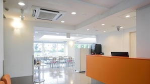 Uma área de recepção com design moderno, incluindo um balcão de atendimento, área de estar com cadeiras e vista para o exterior por grandes janelas.