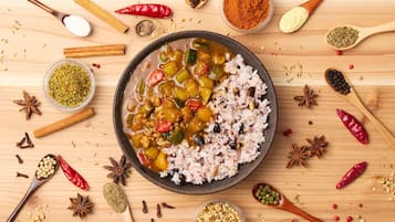 A bowl of rice and vegetable curry surrounded by various spices and ingredients on a wooden surface.