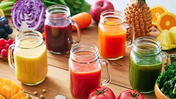 A wooden table with various fruits, vegetables, and three glass jars containing different colored smoothies.