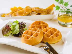 A plate with waffles, a bowl of fruit, a glass of drink, and a salad.