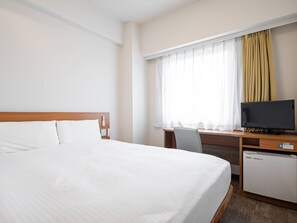 A hotel room with a bed, a desk with a television, and a small refrigerator.