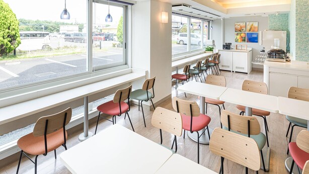 A modern dining area with large windows, multiple tables and chairs, and a kitchen area with appliances. - Comfort Inn Hitachinaka (Hitachinaka)