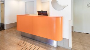 A reception desk with a modern design, a wall-mounted clock, and a door with accessibility symbols. - Comfort Inn Hitachinaka (Hitachinaka)