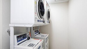 A laundry room with two front-loading washing machines and two dryers on a white shelf. - Comfort Inn Hitachinaka (Hitachinaka)