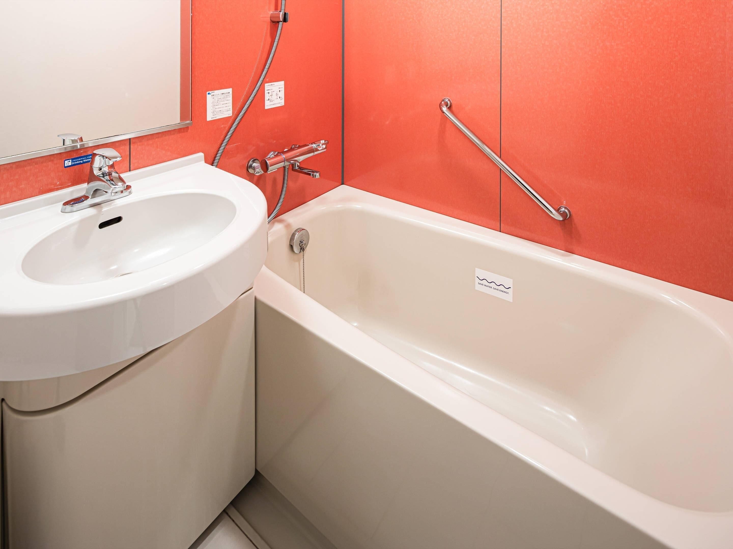 A bathroom with a white sink, a bathtub, and a red wall.