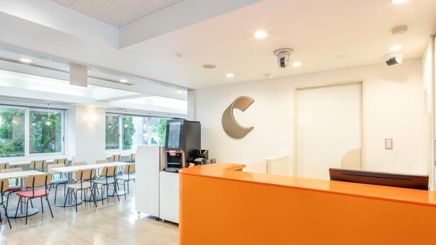 Een moderne receptiebalie met een groot oranje bureau, een digitaal kiosk en een grote, C-vormige wanddecoratie.