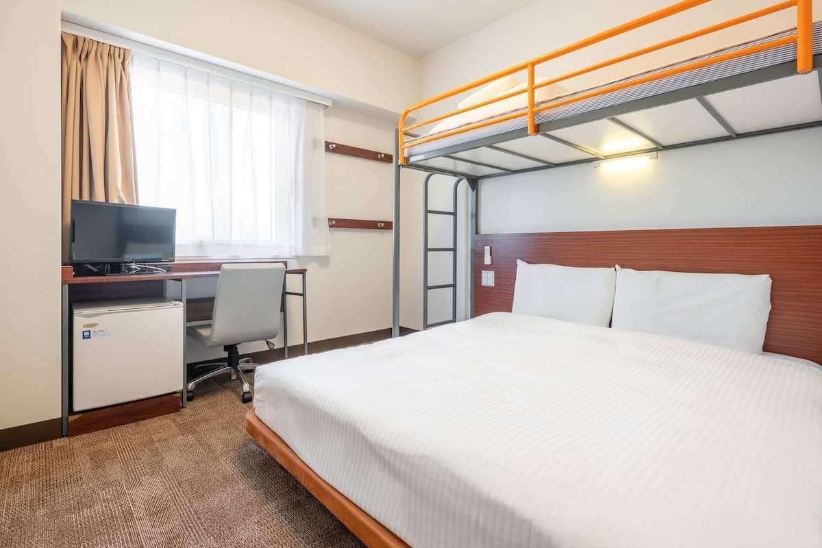 Habitació d'hotel amb lliteres, escriptori amb televisió, cadira i nevera petita.