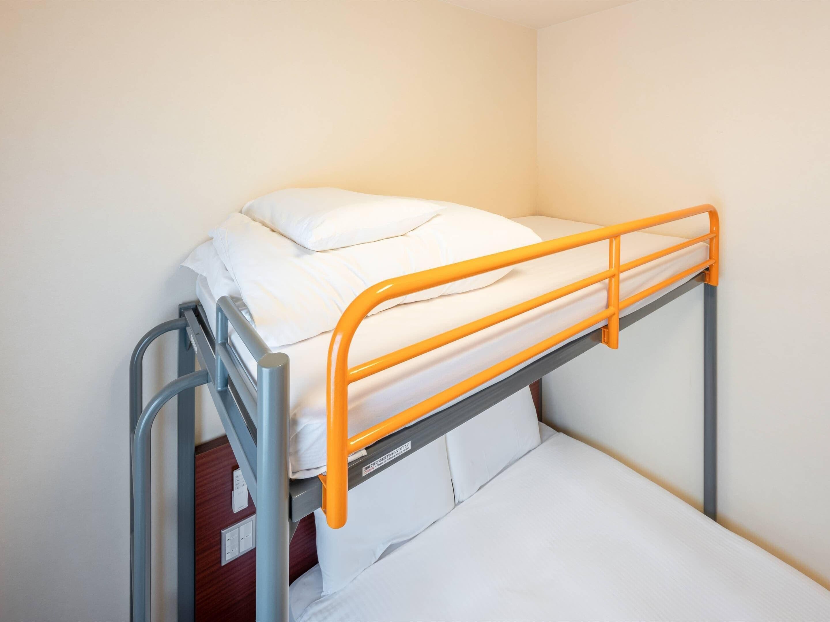 A bunk bed with an orange frame and white bedding in a room with plain walls.