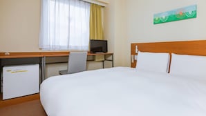 Ein Hotelzimmer mit einem Bett, einem Schreibtisch mit Computer, einem Fernseher und einem kleinen Kühlschrank.