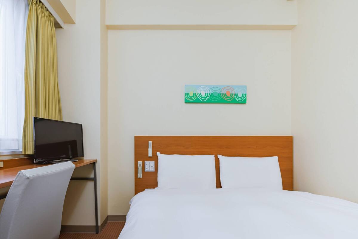 Habitació d'hotel amb un llit, escriptori amb televisió, una cadira i un quadre a la paret.