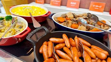 A buffet with various dishes including a red pot of soup, a blue bowl of mixed vegetables, and a black skillet with sausages.