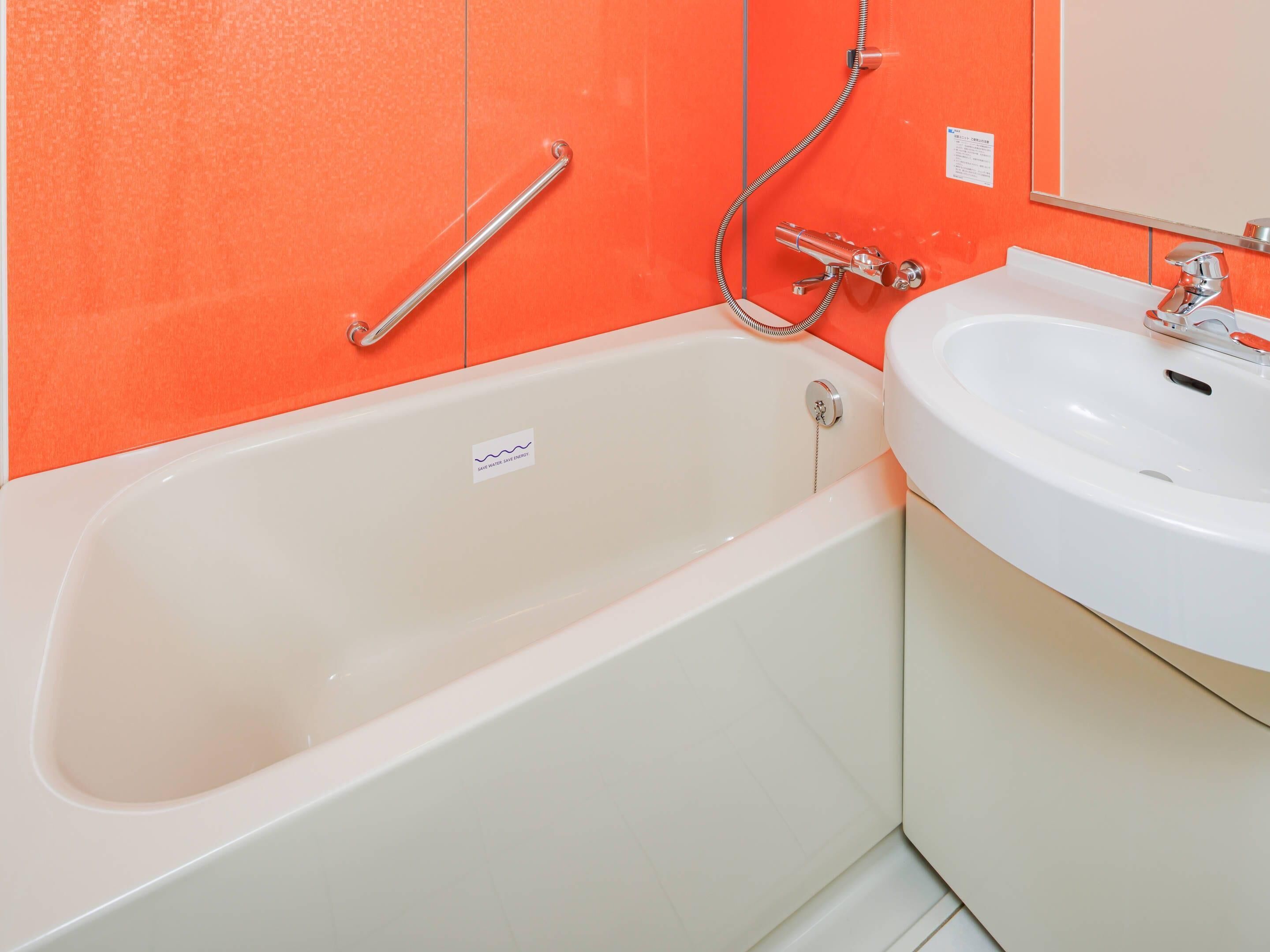 Une salle de bain avec une baignoire blanche, un lavabo blanc et un mur orange.