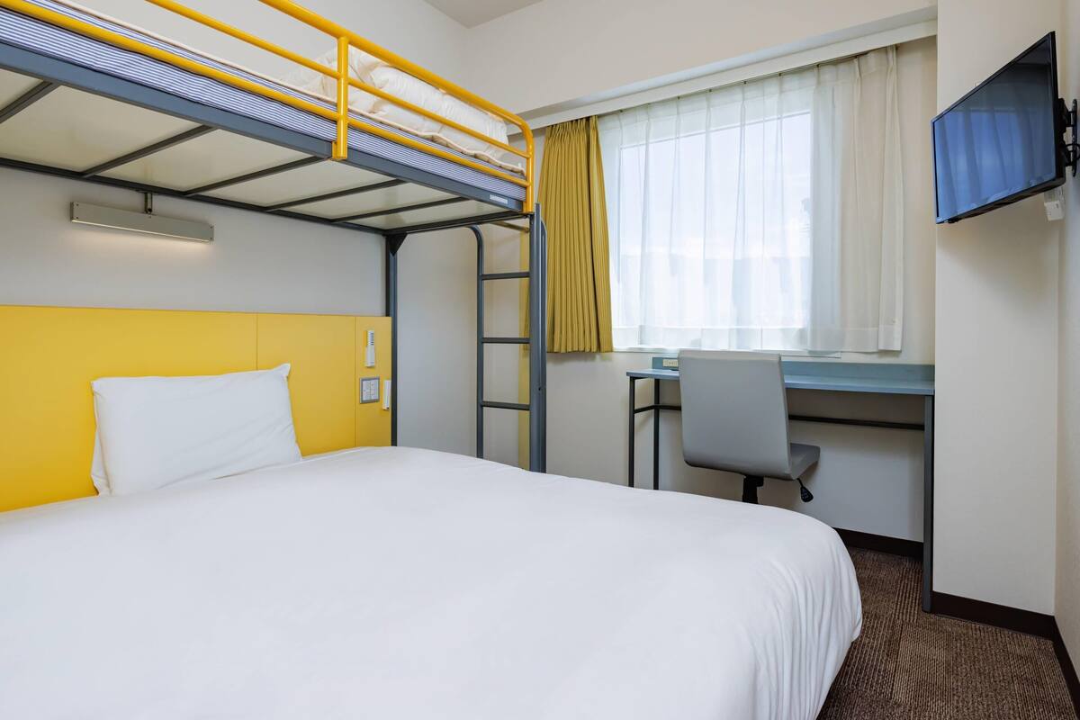 Habitació d'hotel amb lliteres, escriptori, cadira i televisió.