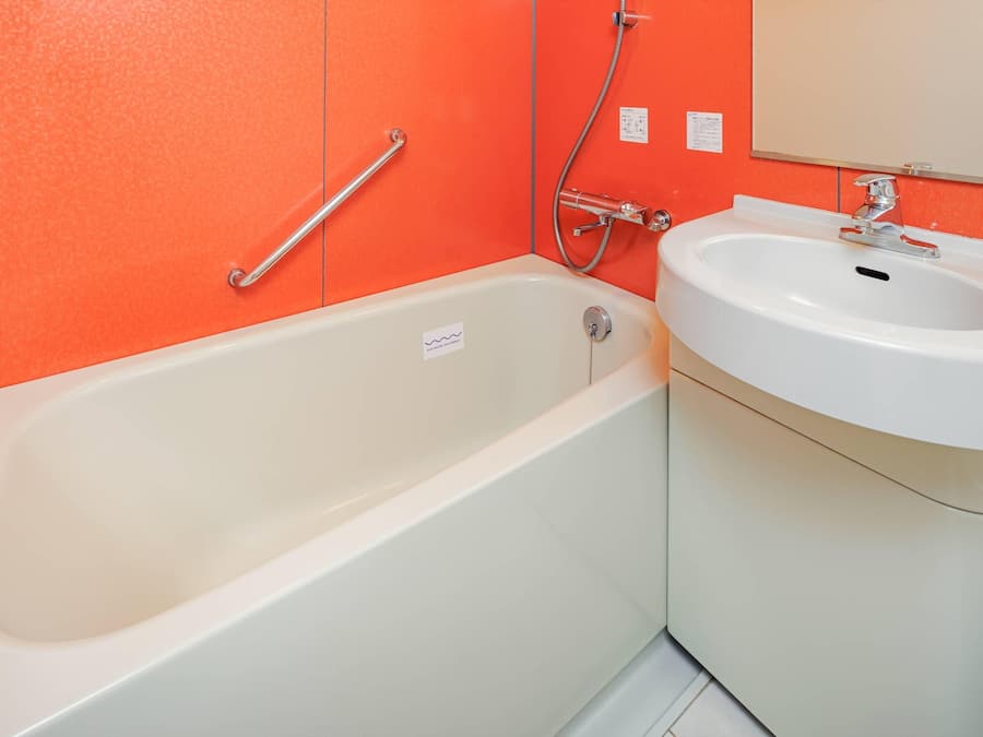 A bathroom with a white bathtub, a white sink, and an orange wall.