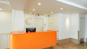A reception area with an orange desk, a clock on the wall, and a door in the background. - Comfort Inn Kofu Isawa (Fuefuki)