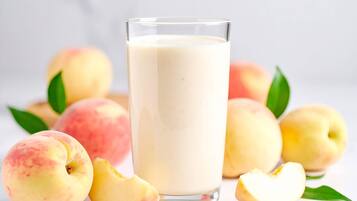 A glass of milk with peaches and leaves around it.