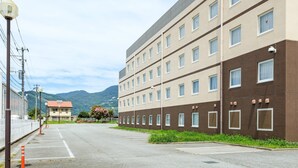 A multi-story hotel with a parking lot in front, surrounded by greenery and mountains in the background. - Comfort Inn Kofu Isawa (Fuefuki)
