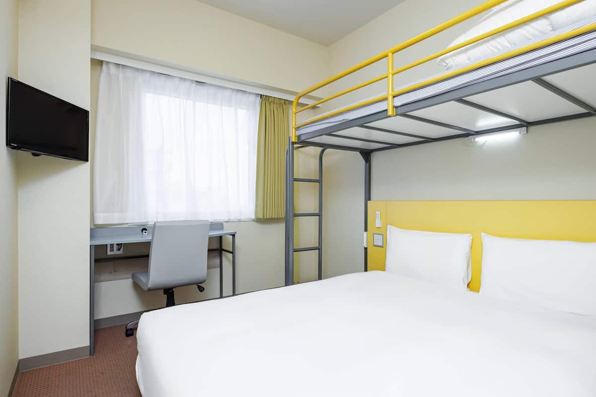 A hotel room with a bunk bed, a desk with a chair, a television, and a window with curtains.