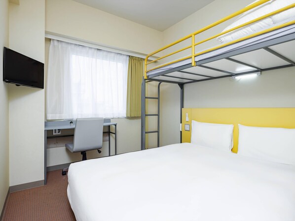 A hotel room with a bunk bed, a desk with a chair, a television, and a window with curtains.