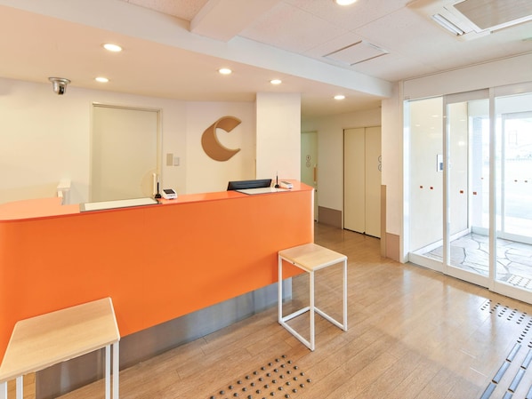 A reception area with an orange counter, a white chair, a small wooden stool, and a crescent moon decoration on the wall. - Comfort Inn Ichinoseki Inter (Ichinoseki)