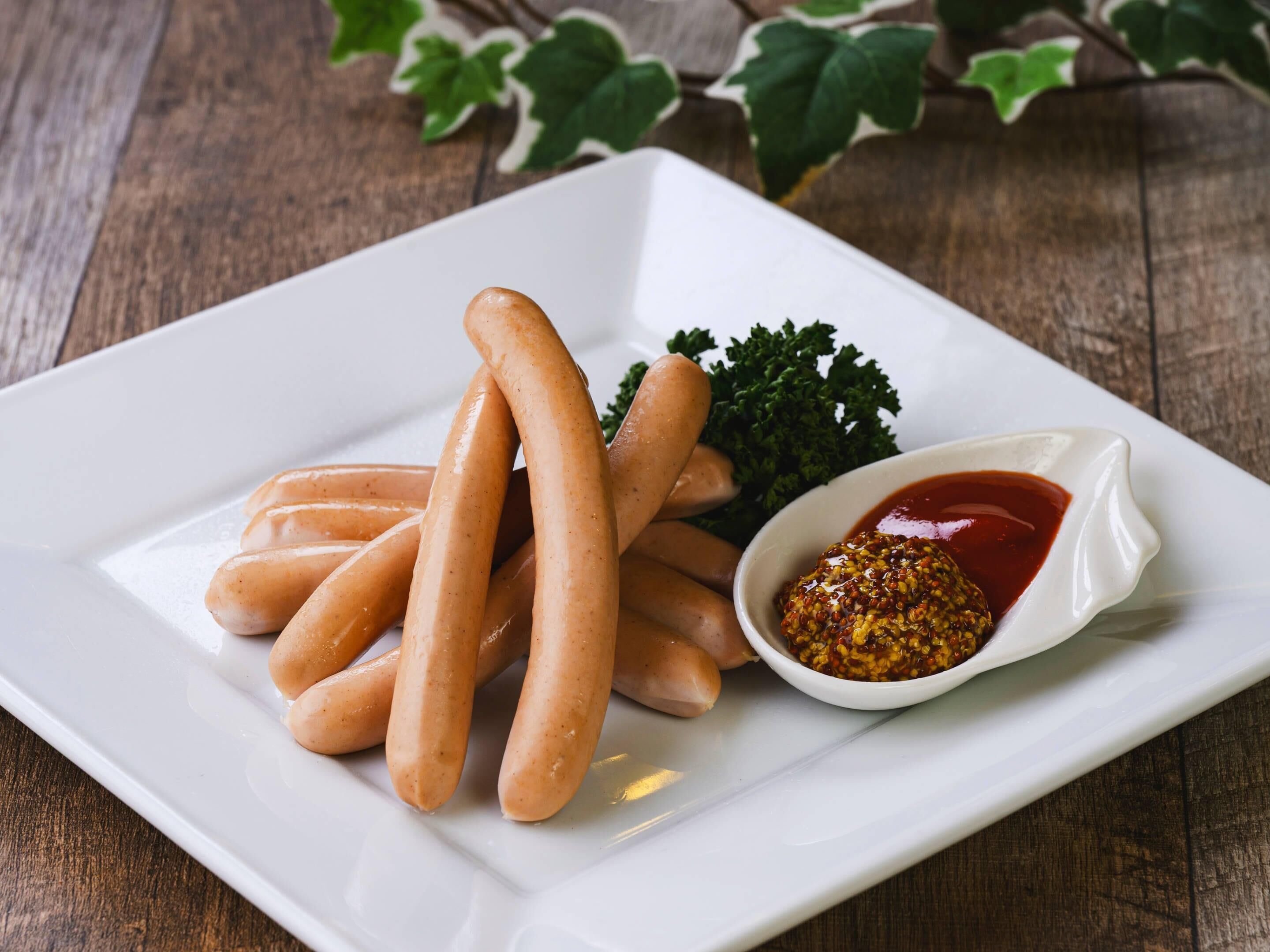 A white plate with several sausages and a small bowl of mustard.