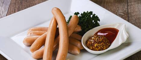 A white plate with several sausages and a small bowl of mustard.