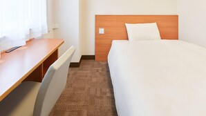 Hotellihuone, jossa on puinen työpöytä, valkoisilla lakanoiden peitetty sänky ja ruskea matto.