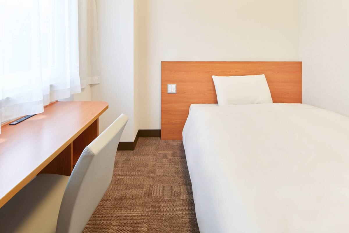 Ein Hotelzimmer mit einem Holztisch, einem Bett mit weißer Bettwäsche und einem braunen Teppich.