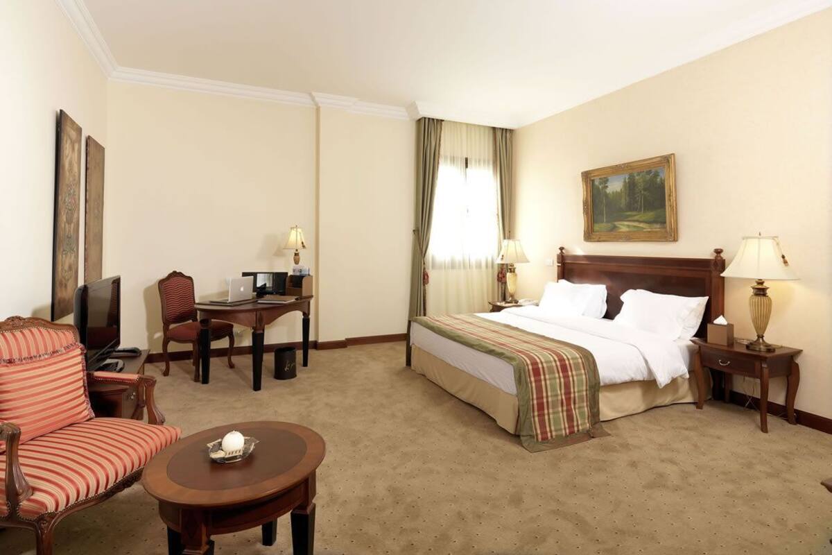 Una habitación de hotel con cama, escritorio, silla, televisor y lámpara.