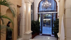 Una entrada majestuosa con candelabro, columnas y plantas en macetas.