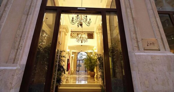 A grand entrance with a chandelier, a flag, and a sign reading "le patio".