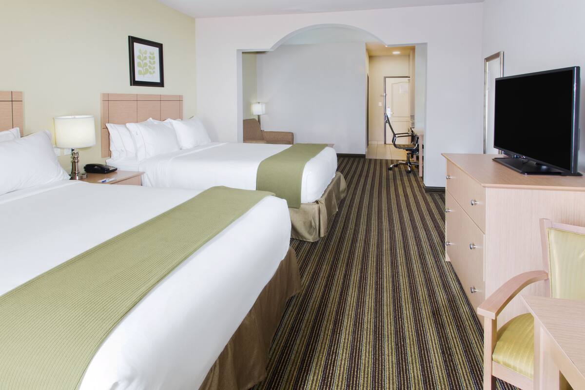 A hotel room with two beds, a television, a desk, and a chair.