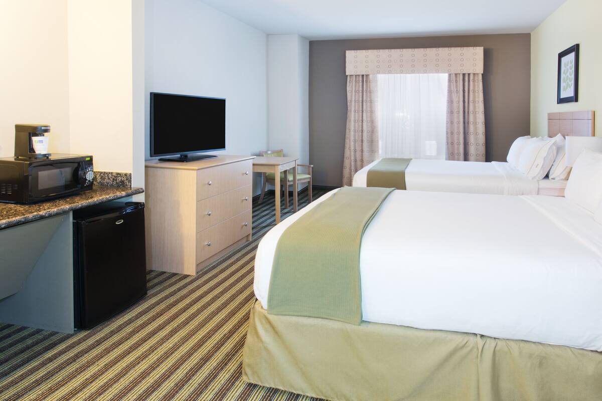 A hotel room with a bed, a desk, a television, a microwave, and a refrigerator.