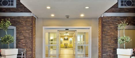 A hotel entrance with a brick facade, double doors, and a tiled entrance area.