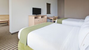 Ein Hotelzimmer mit zwei Betten, einem Schreibtisch, einem Fernseher, einem Sessel und einem kleinen Fenster.