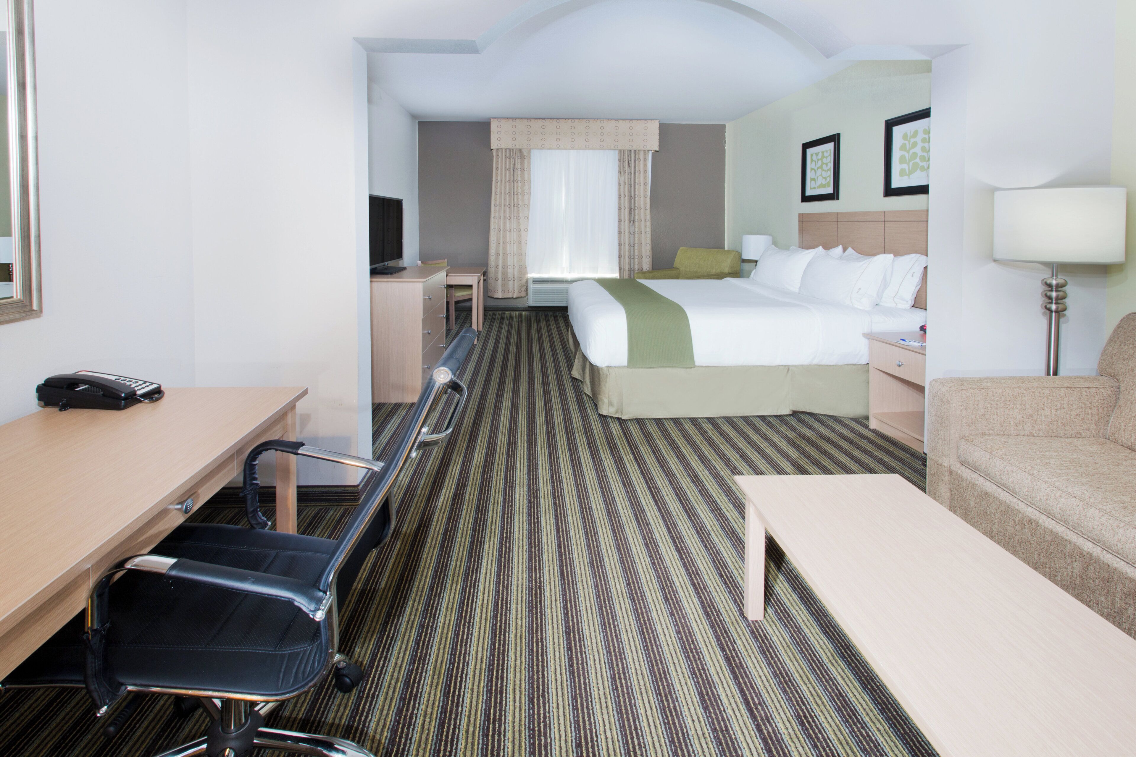 Une chambre d’hôtel avec un lit, un bureau, une chaise, un canapé et une lampe.