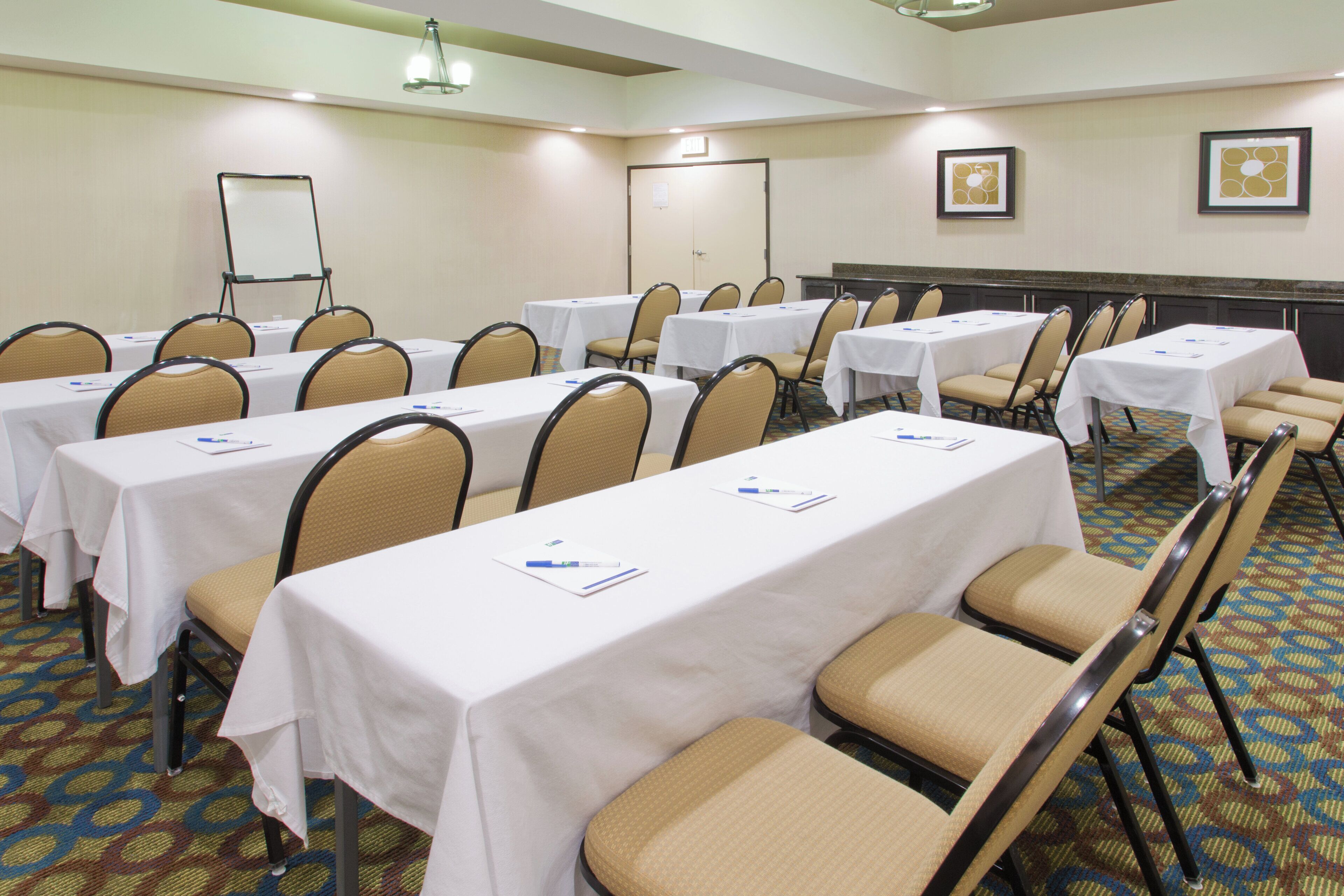 A conference room with multiple tables and chairs, white tablecloths, and a carpeted floor.