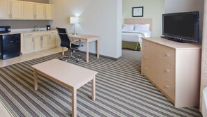 Ein Hotelzimmer mit Küchenzeile, einem Bett, einem Fernseher, einem Schreibtisch und einem Stuhl.