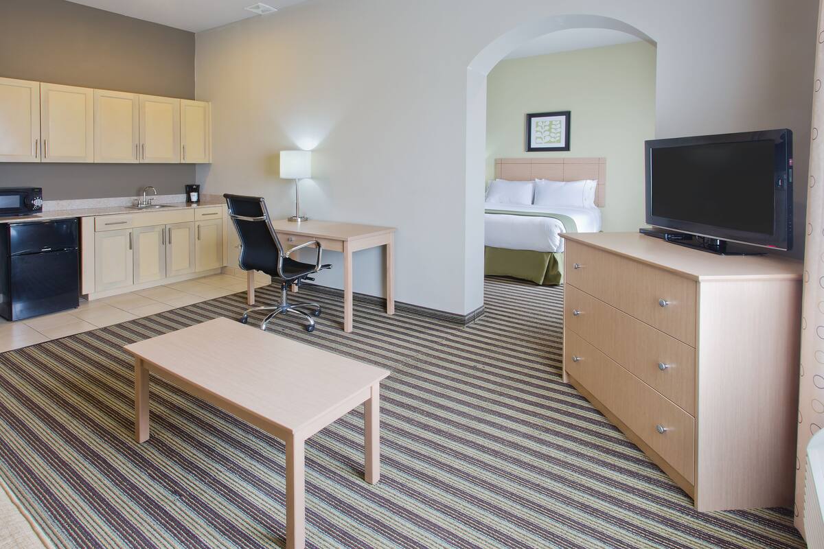 A hotel room with a kitchenette, a bed, a TV, a desk, and a chair.