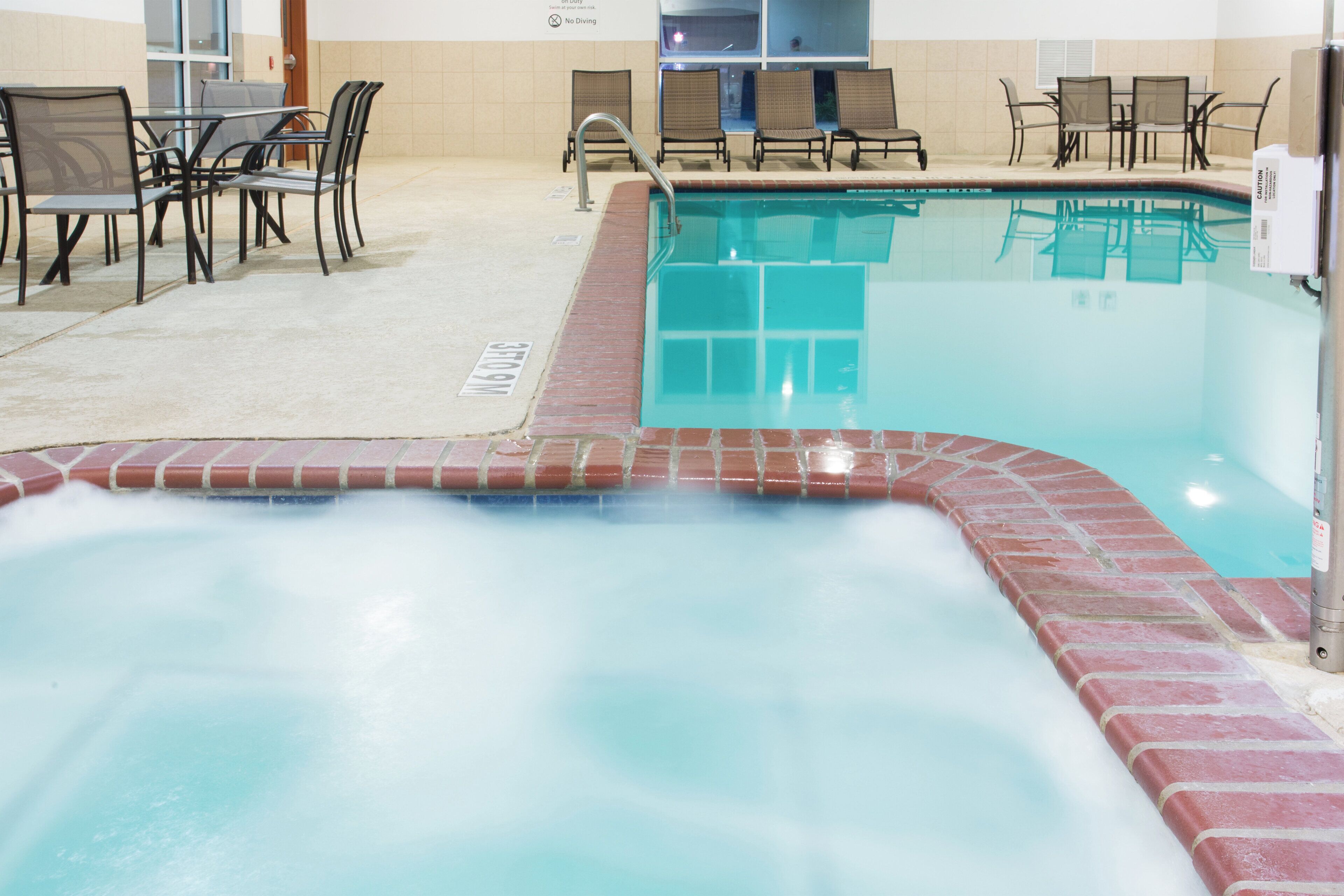 Una piscina con jacuzzi, rodeada de sillas y mesas de descanso.