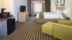 Ein Hotelzimmer mit einem Bett, einem Schreibtisch mit Computer, einem Fernseher, einer Mikrowelle, einem kleinen Kühlschrank und einer Sitzecke mit zwei Sesseln.