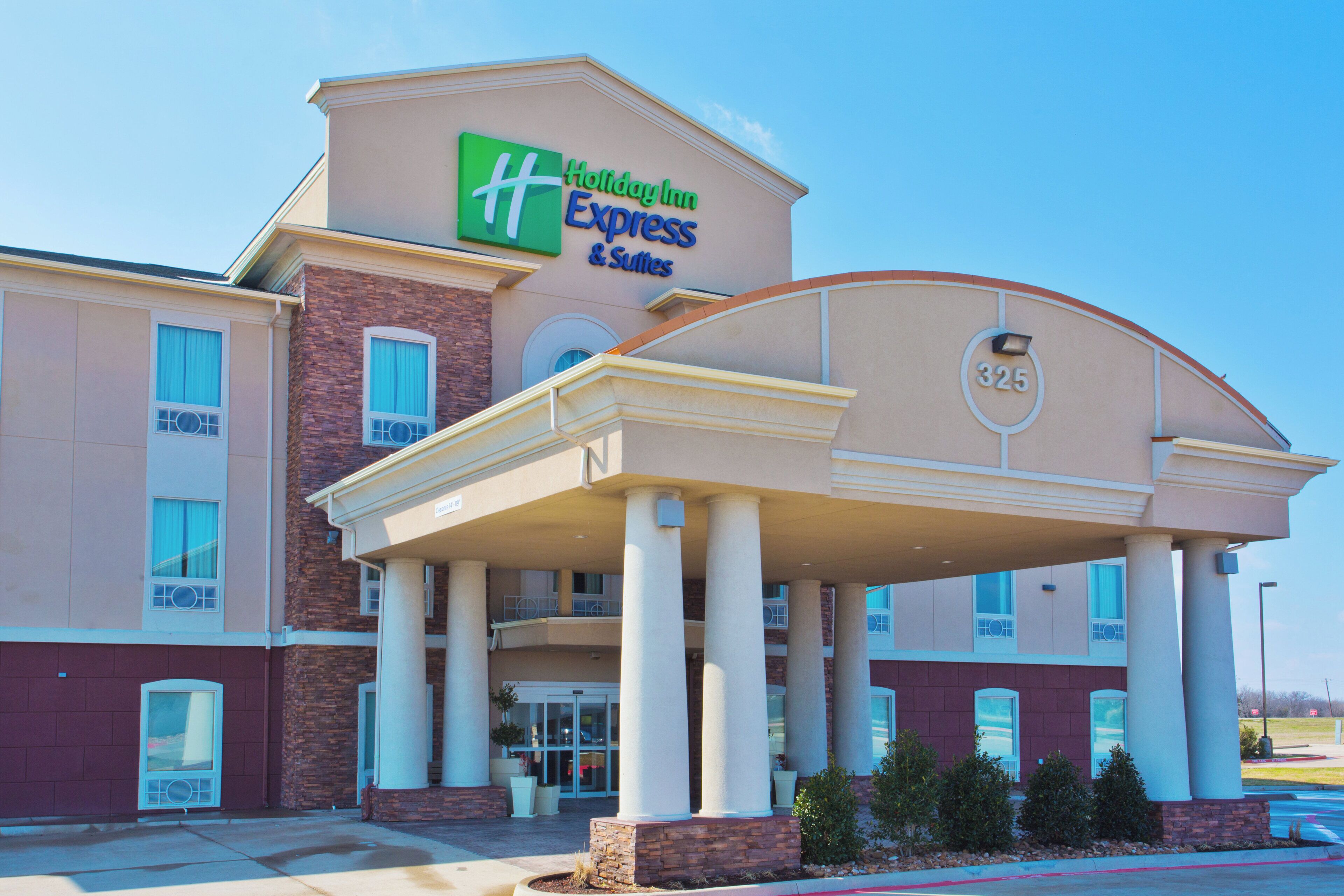 A Holiday Inn Express & Suites building with a covered entrance, columns, and a brick facade.