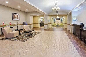 A hotel lobby with a reception desk, seating area, and a dining space.
