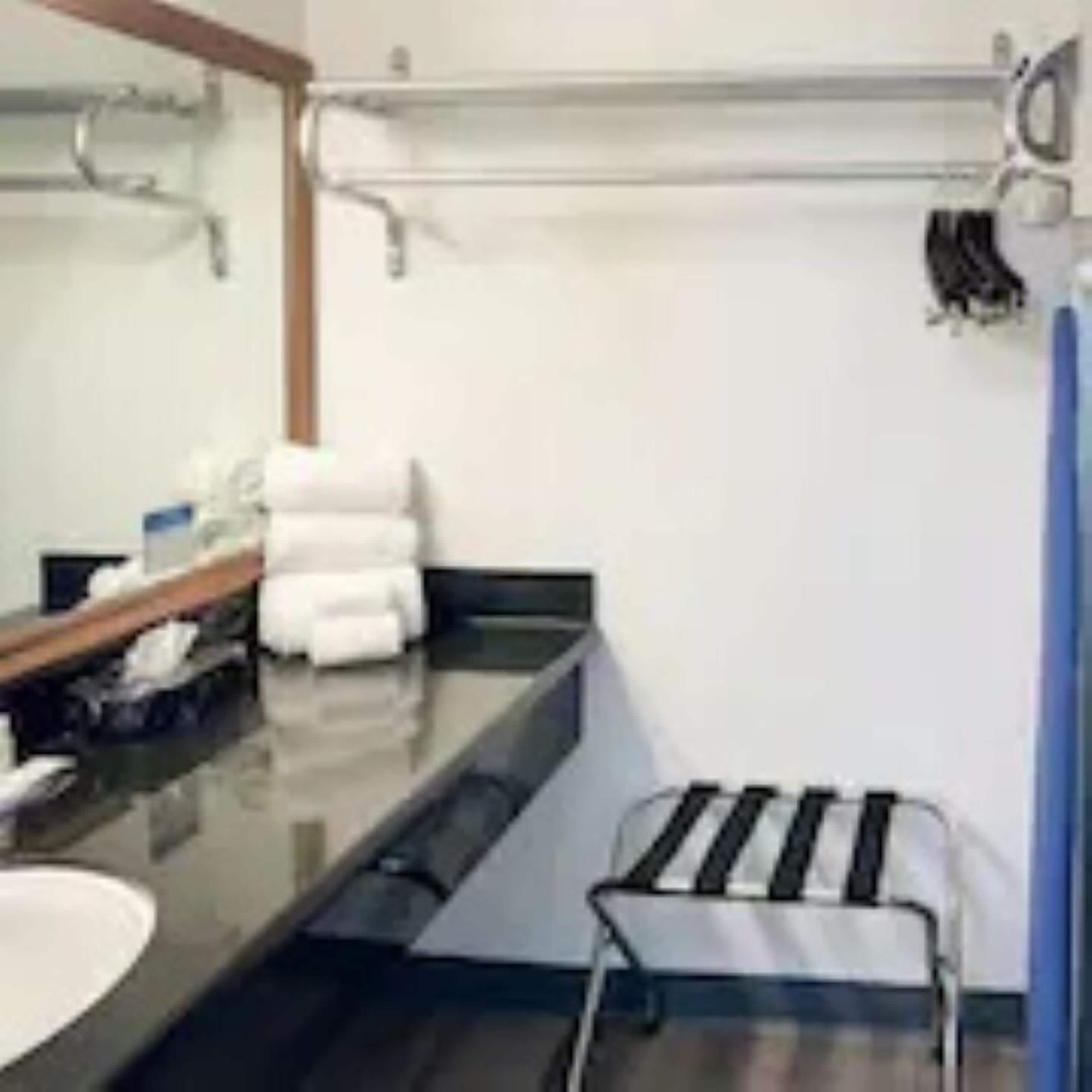 Une salle de bain équipée d’un lavabo, d’un miroir, d’un porte-serviettes et d’un petit tabouret.