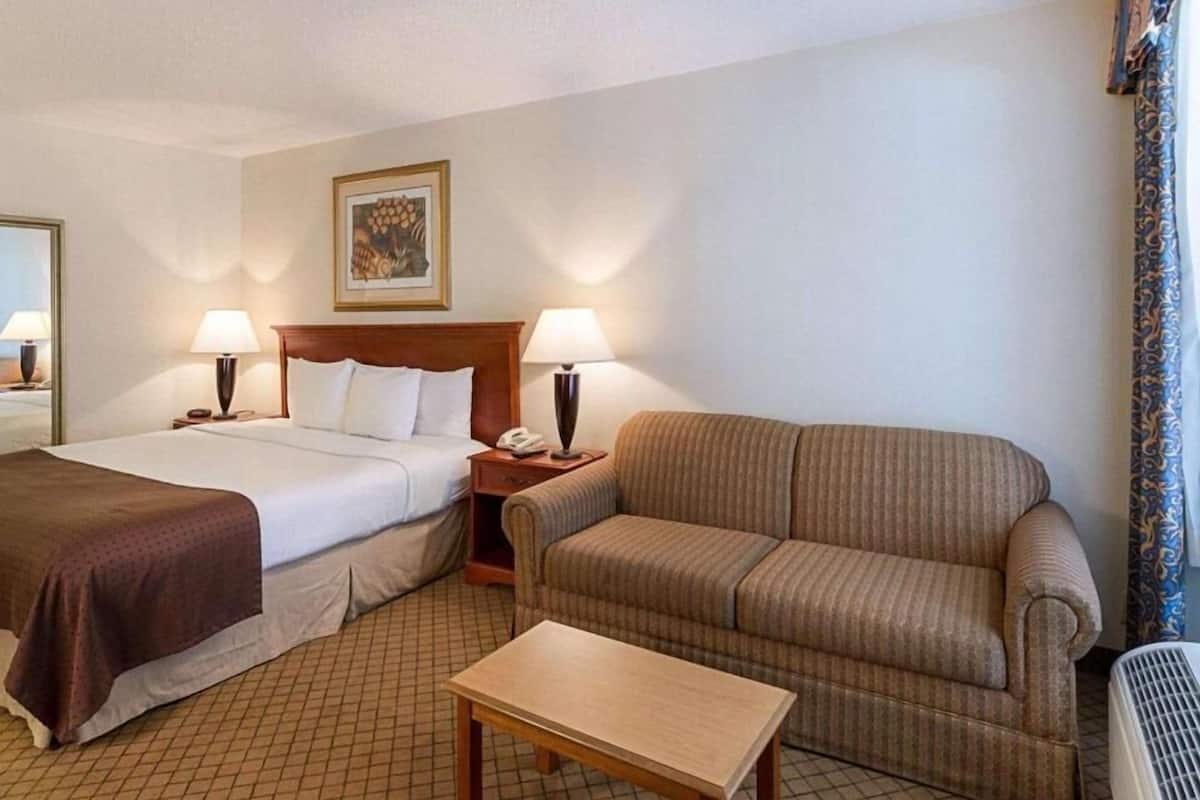 Une chambre d’hôtel avec deux lits, un canapé, une petite table et une table de chevet avec une lampe.