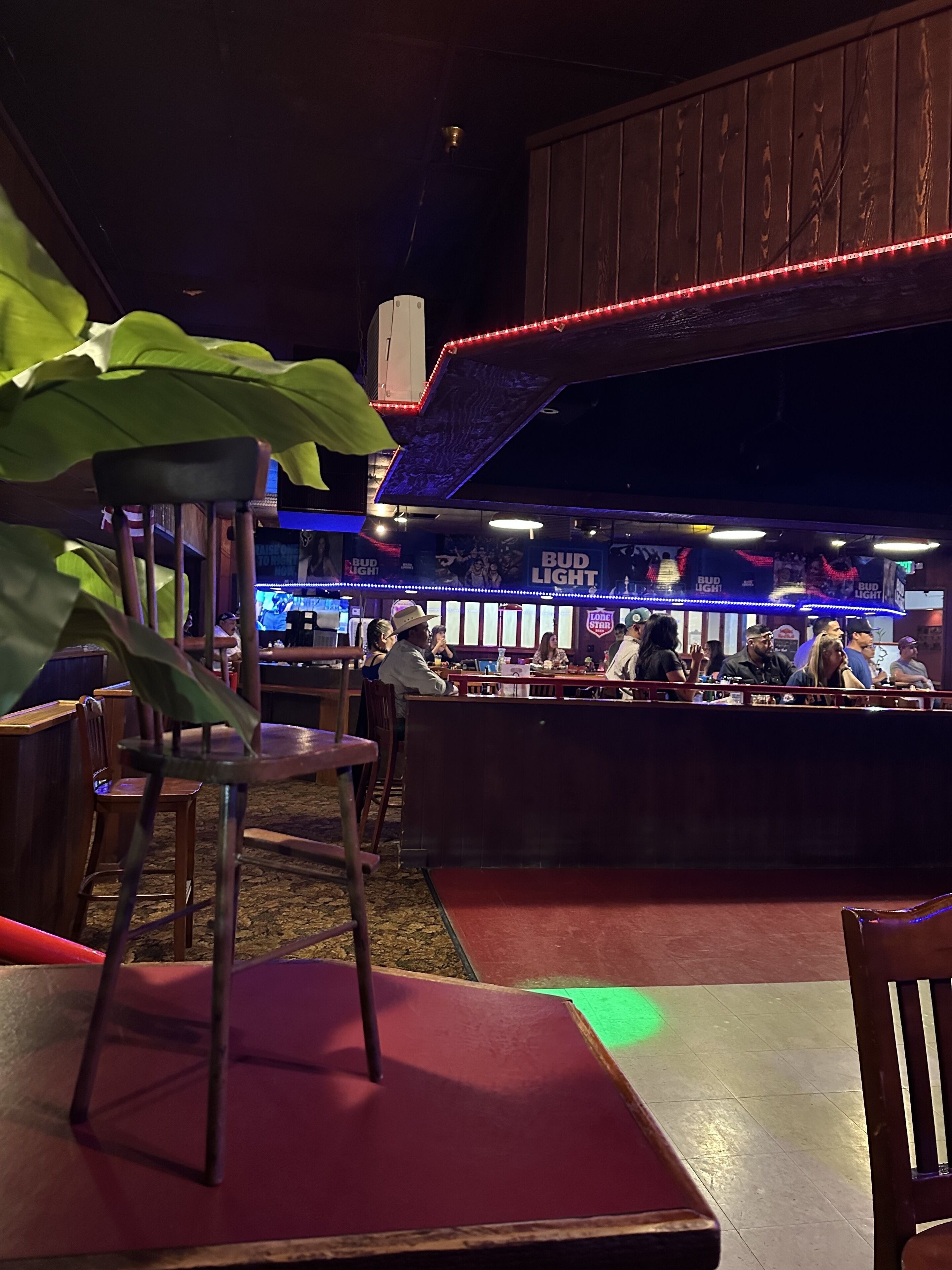 Un bar intérieur avec des meubles en bois, un comptoir où sont assis des clients et une enseigne « BUD LIGHT ».