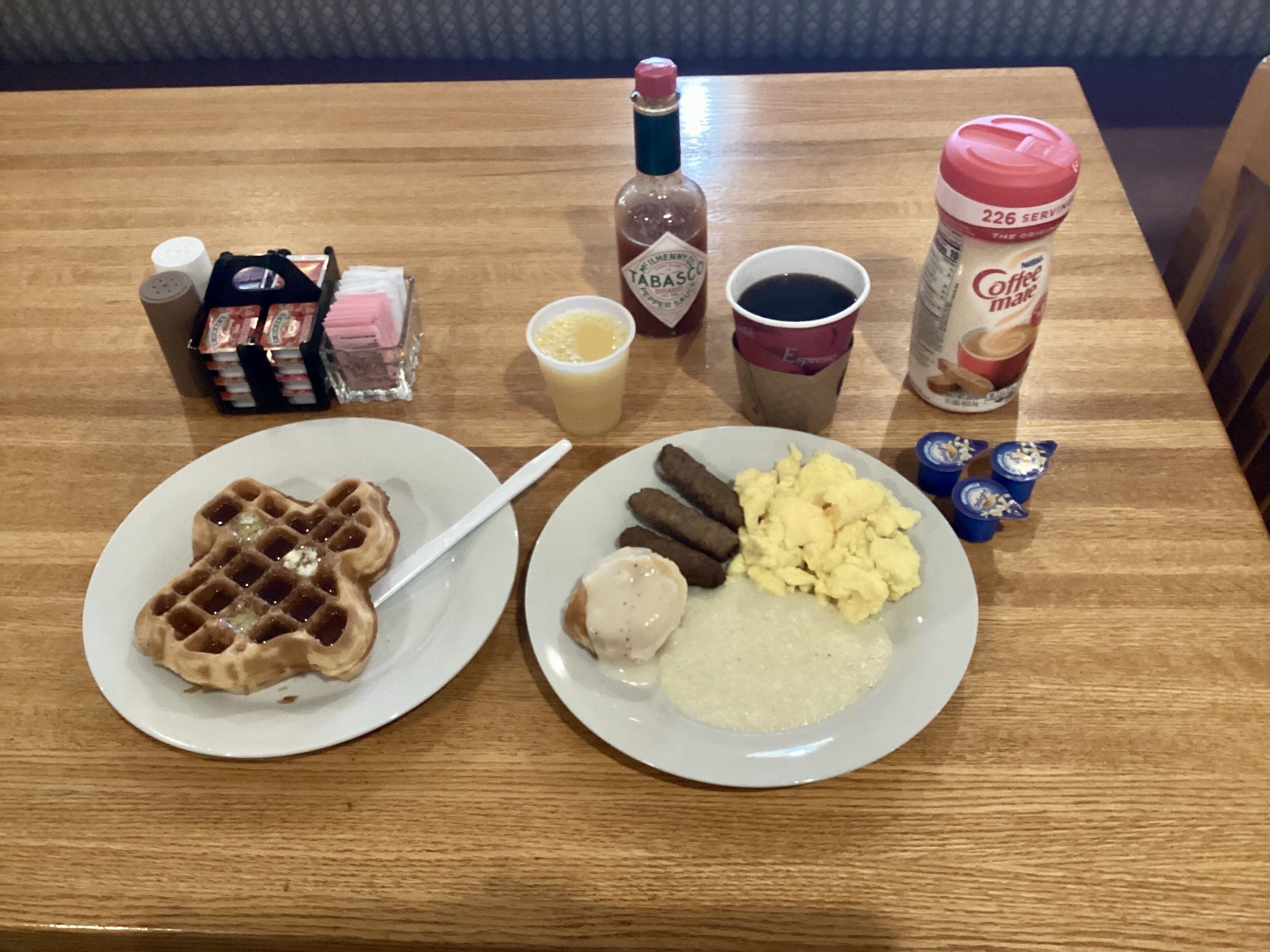 Een tafel met ontbijtartikelen zoals wafels, worstjes, roerei en koffie.