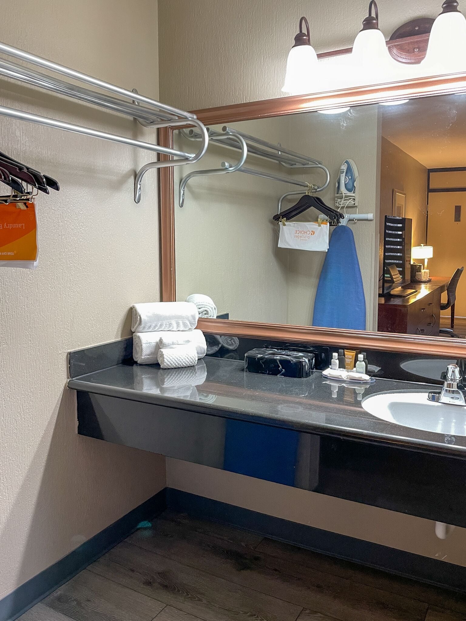 A bathroom with a large mirror, a sink, and a towel rack. There are towels and toiletries on the counter.