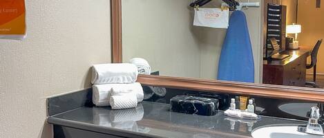 A bathroom with a large mirror, a sink, and a towel rack. There are towels and toiletries on the counter.